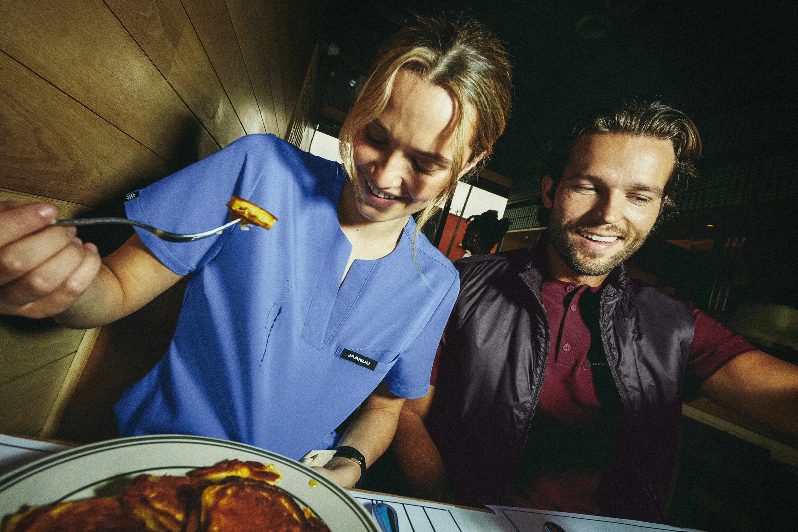 Woman in scrubs happily eating a meal with a man beside her.