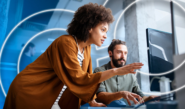Professional woman explaining something on a monitor to a coworker during a collaborative work session.