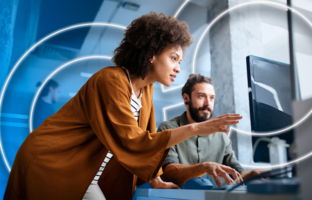 Professional woman explaining something on a monitor to a coworker during a collaborative work session.